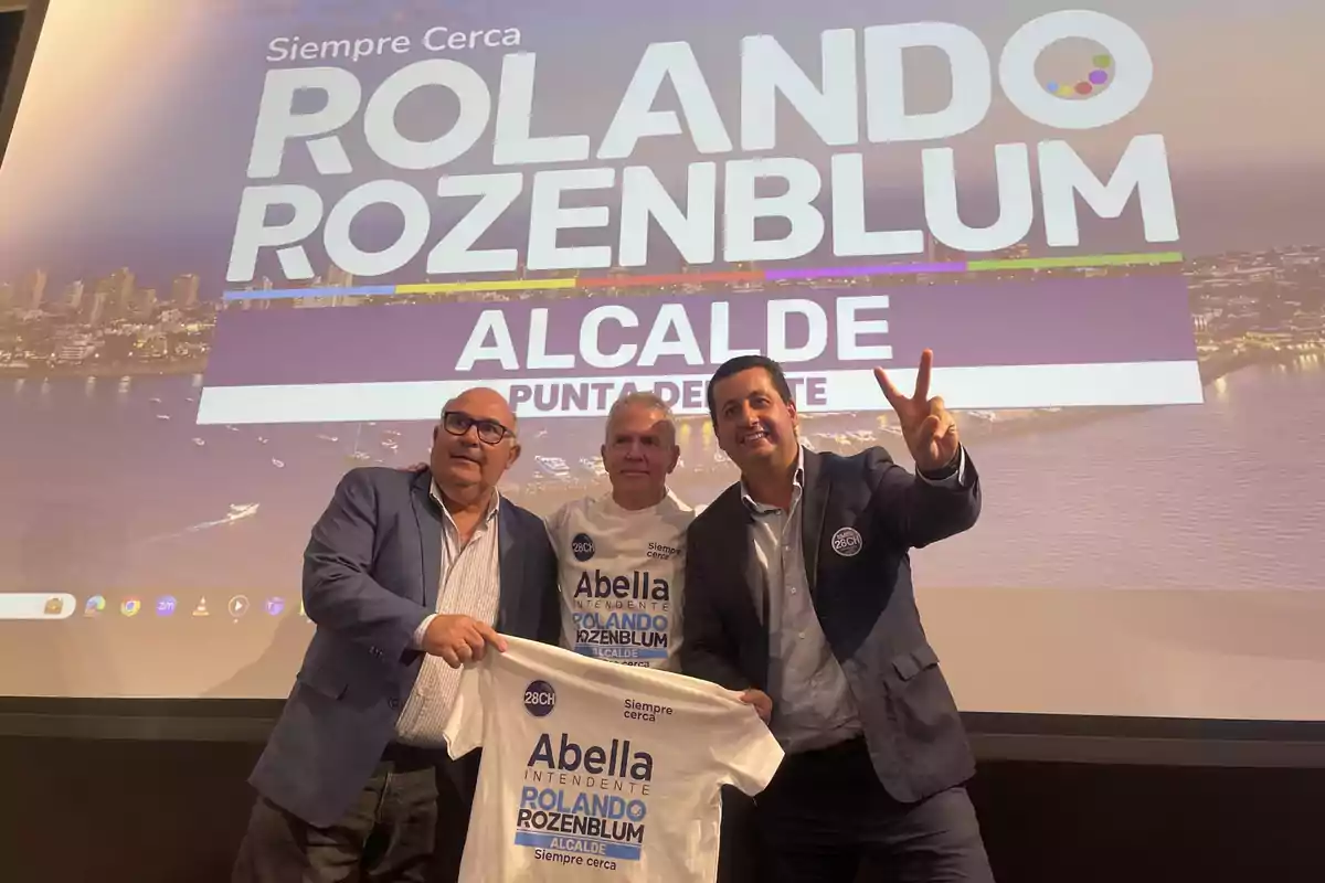 Tres personas posan frente a un cartel de campaña política que dice Tres personas posan frente a un cartel de campaña política que dice