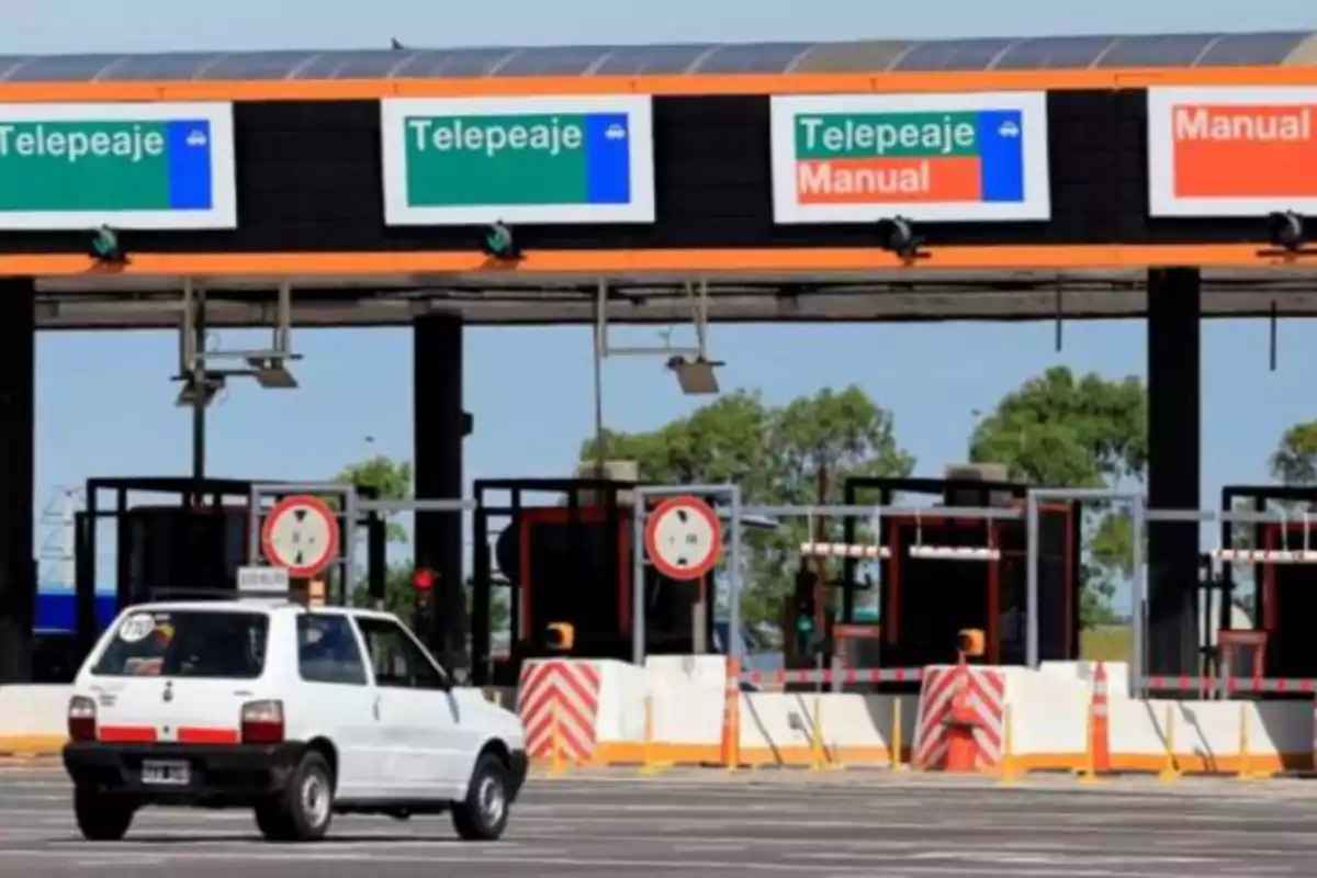 Un automóvil blanco se aproxima a una cabina de peaje con señales que indican telepeaje y pago manual en la Ruta 2 a la costa atlántica.