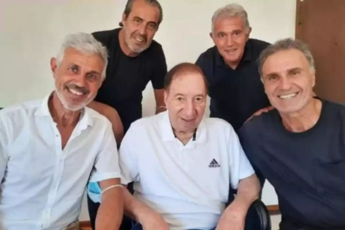 Five smiling men pose together for a photo in an indoor setting.