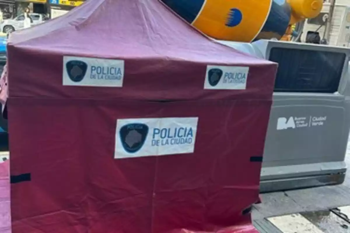 A red tent with the City Police logo is set up on a street next to a garbage container.