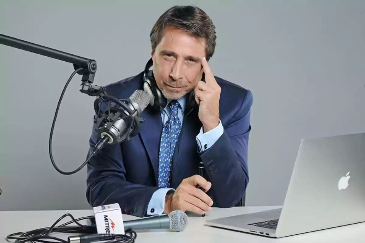 Un hombre en traje azul con auriculares y micrófono frente a una computadora portátil.