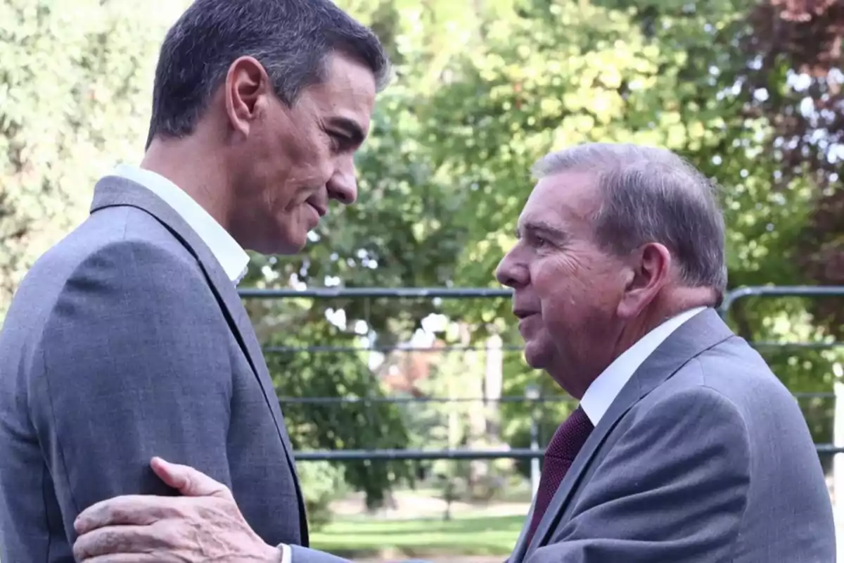 Dos hombres de traje conversando al aire libre.