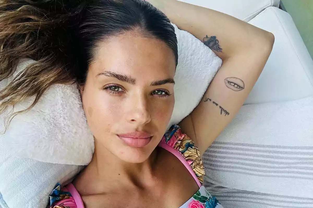 Mujer recostada con tatuajes visibles en el brazo y cabello suelto.