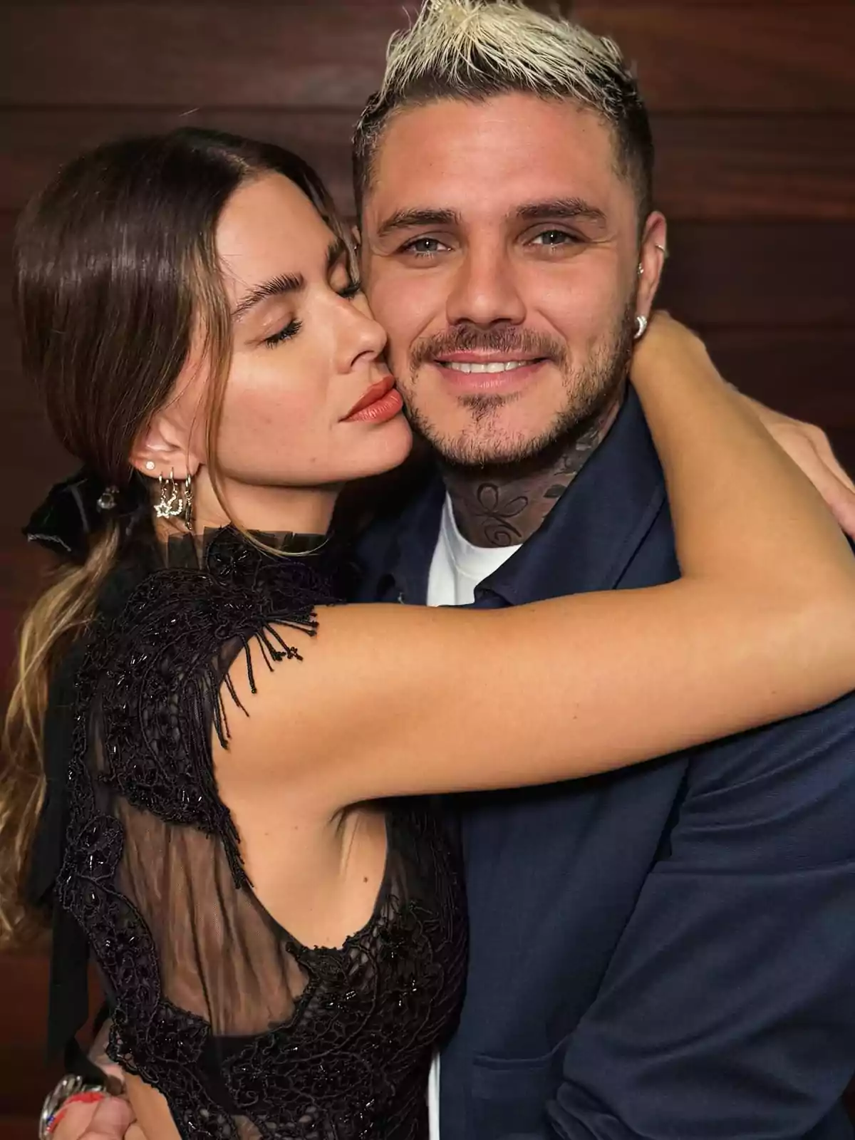 Una pareja abrazándose con expresiones de afecto, ella con los ojos cerrados y él sonriendo, ambos vestidos de manera elegante. Una pareja abrazándose con expresiones de afecto, ella con los ojos cerrados y él sonriendo, ambos vestidos de manera elegante.