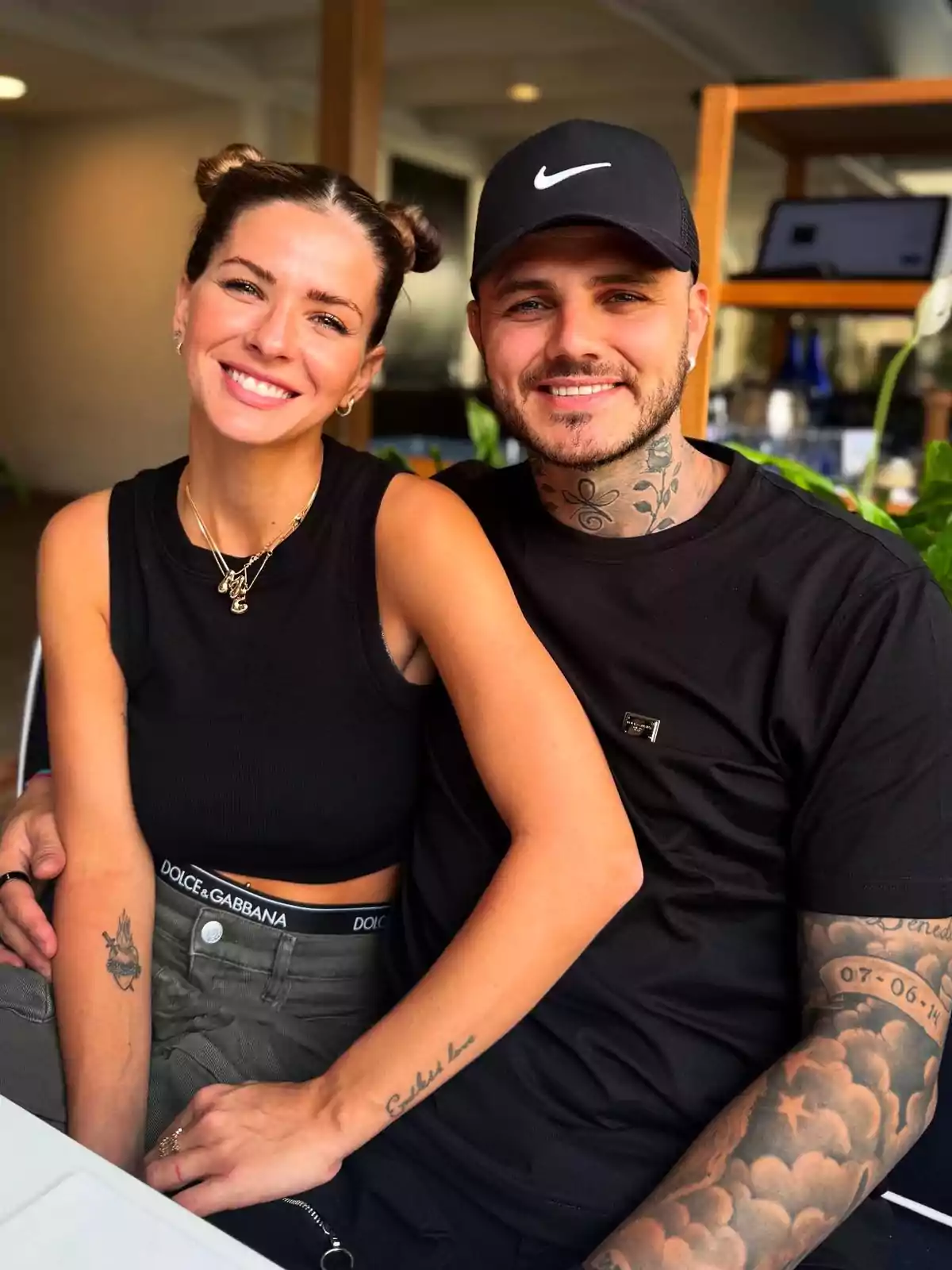 Una pareja sonriente posa para la cámara en un ambiente interior, ambos visten ropa casual y tienen tatuajes visibles. Una pareja sonriente posa para la cámara en un ambiente interior, ambos visten ropa casual y tienen tatuajes visibles.