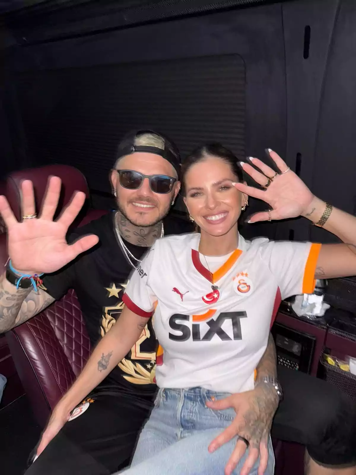 A smiling couple sitting in a vehicle, both raising a hand in greeting. A smiling couple sitting in a vehicle, both raising a hand in greeting.