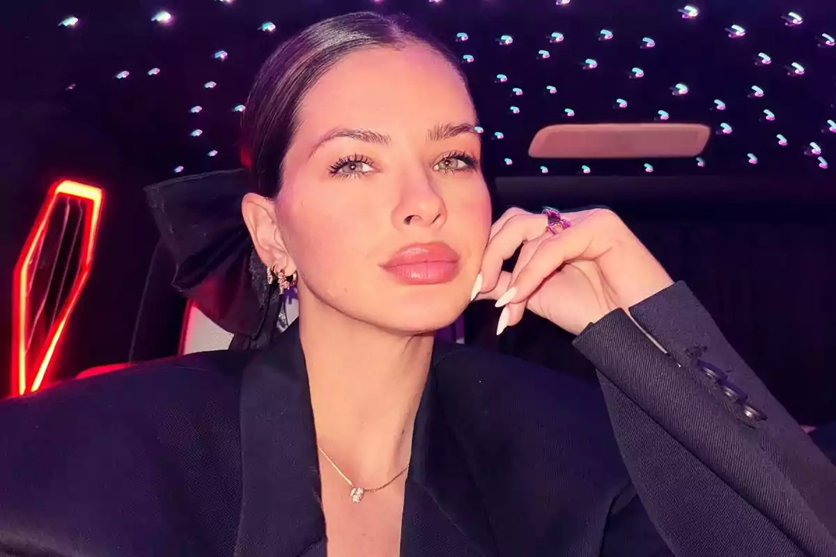 Woman with her hair up and made-up lips posing inside a car with colored lights on the ceiling