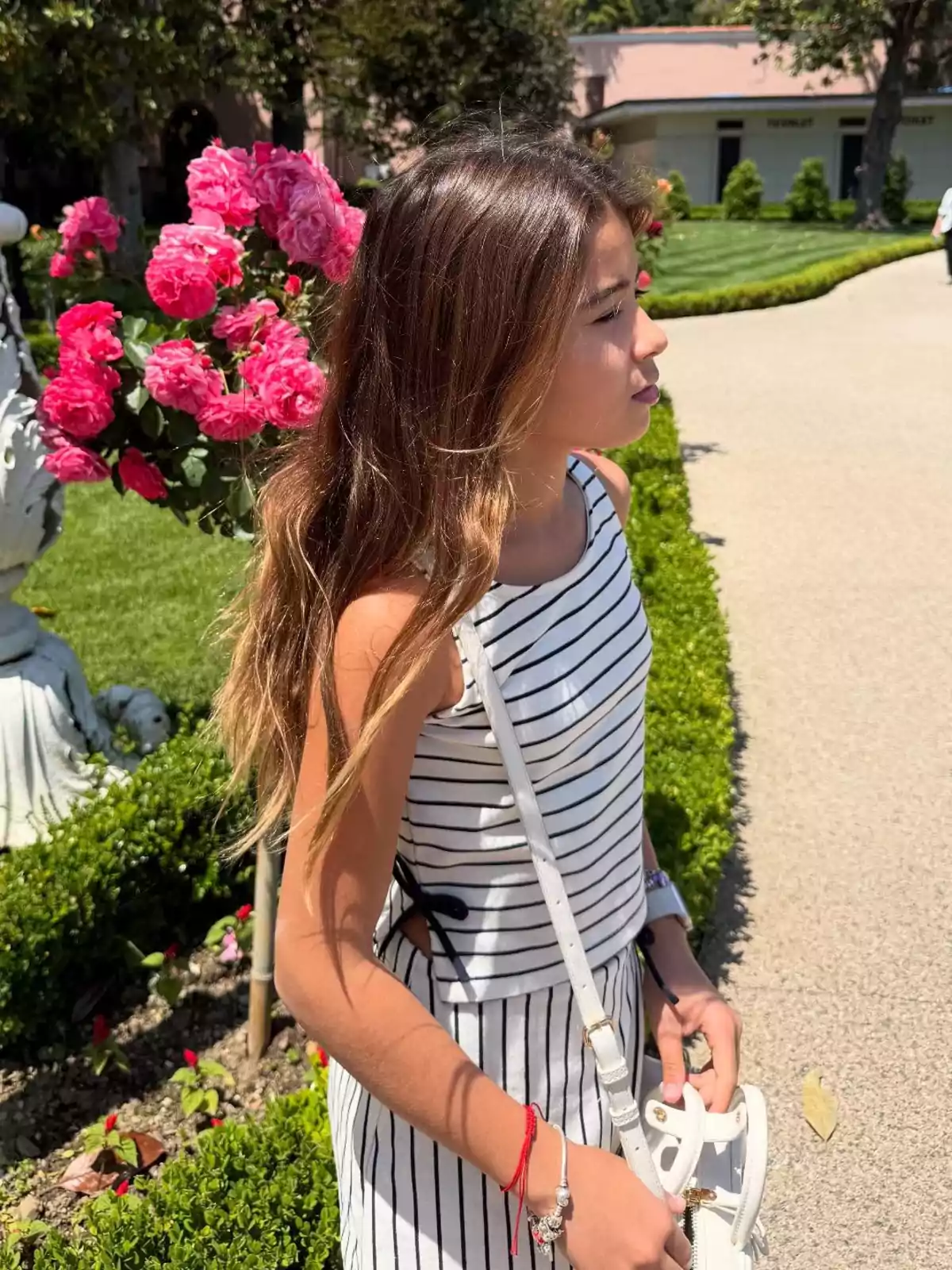 Young woman in a black and white striped dress walking through a garden with pink flowers and trimmed bushes on a sunny day Young woman in a black and white striped dress walking through a garden with pink flowers and trimmed bushes on a sunny day