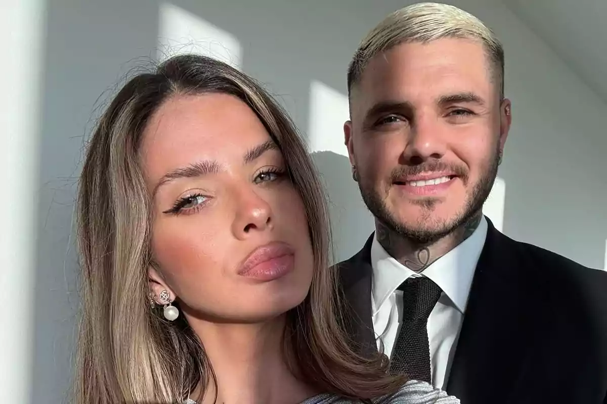 Una mujer y un hombre posan juntos para una selfie con luz natural entrando por una ventana ambos lucen elegantes y sonrientes