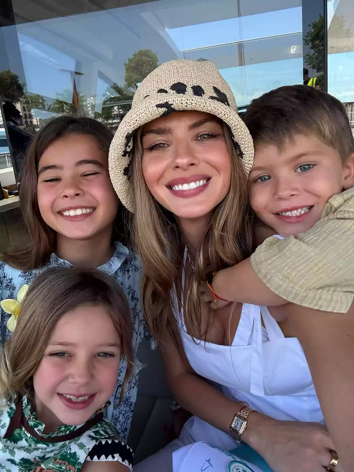 Una mujer sonriente con sombrero claro posa junto a tres niños que también sonríen, todos parecen estar disfrutando de un momento juntos al aire libre. Una mujer sonriente con sombrero claro posa junto a tres niños que también sonríen, todos parecen estar disfrutando de un momento juntos al aire libre.