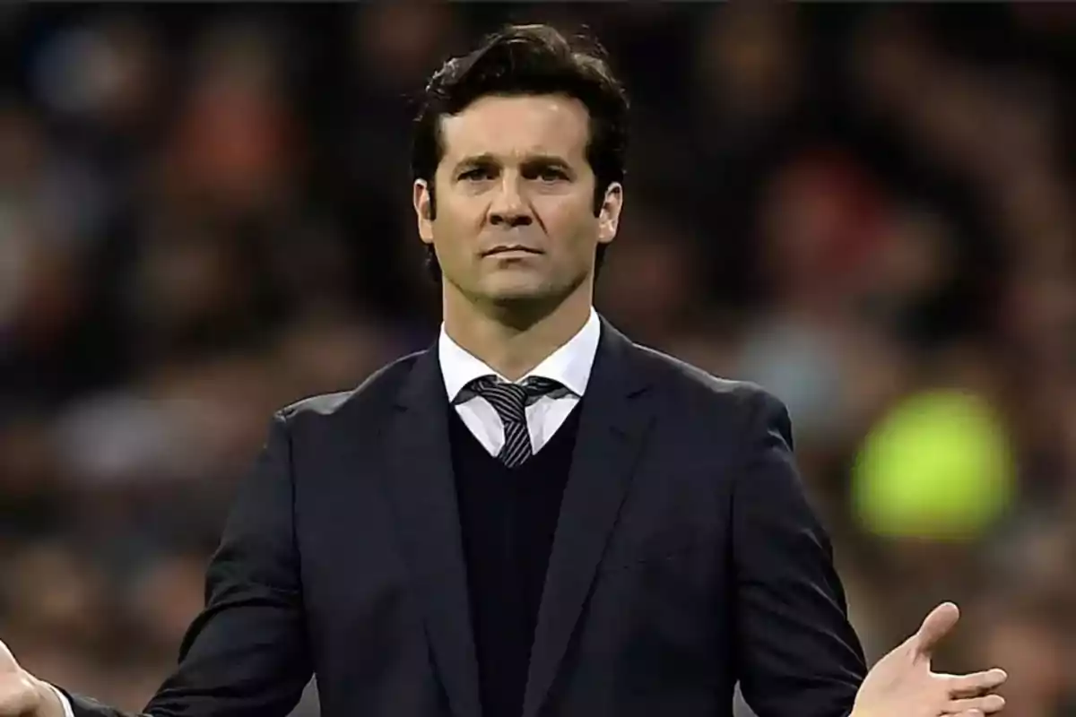 Hombre de cabello oscuro con traje y corbata en un estadio con expresión seria y los brazos extendidos Hombre de cabello oscuro con traje y corbata en un estadio con expresión seria y los brazos extendidos