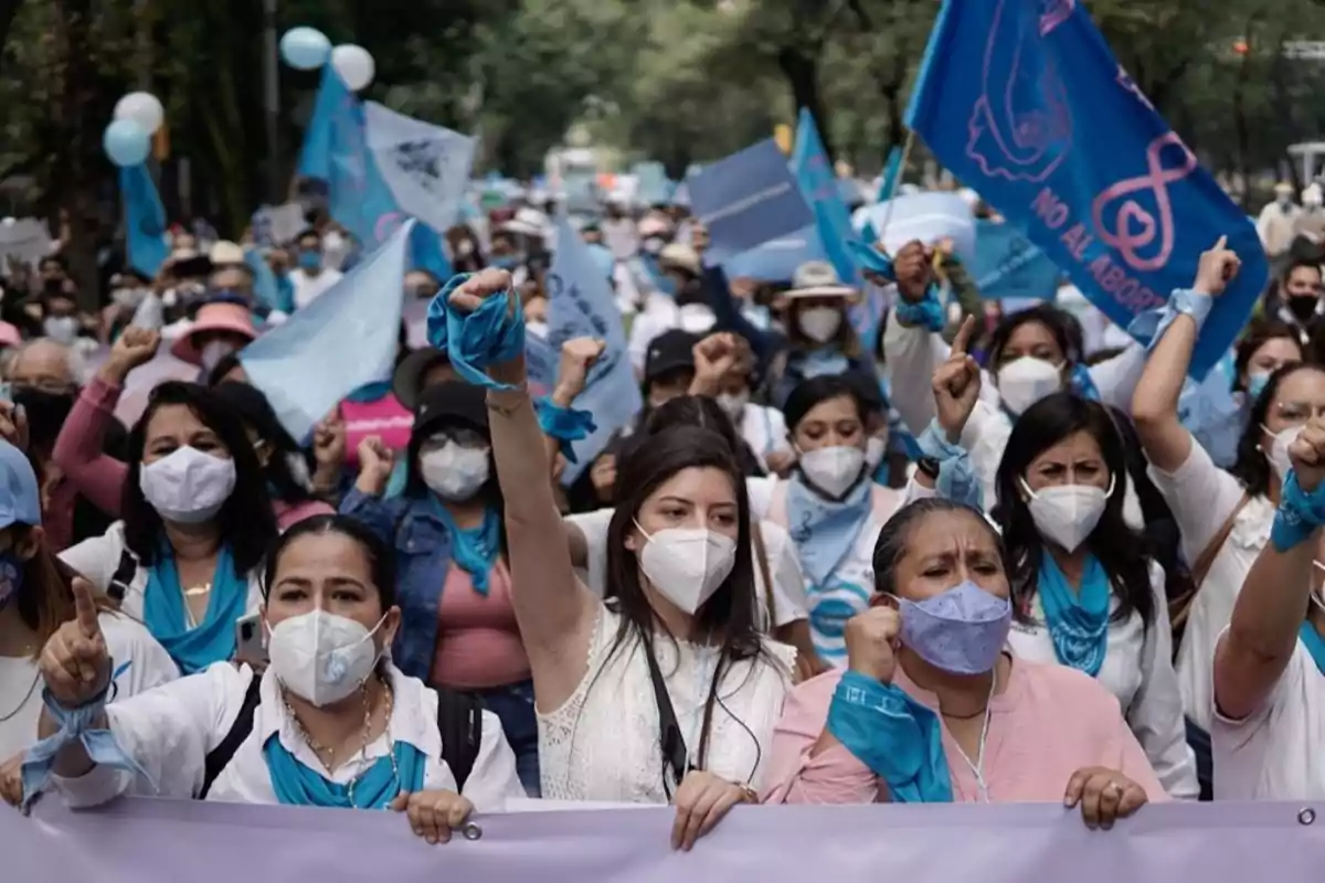 A group of people with masks and blue bandanas participates in a demonstration, raising their fists and carrying flags. A group of people with masks and blue bandanas participates in a demonstration, raising their fists and carrying flags.