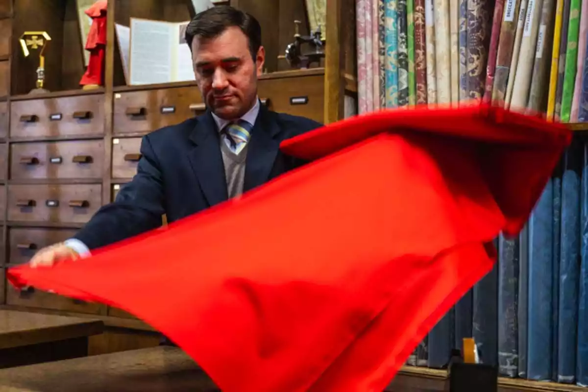 A man in a fabric store holding a red fabric in front of a background of shelves with rolls of fabric. A man in a fabric store holding a red fabric in front of a background of shelves with rolls of fabric.