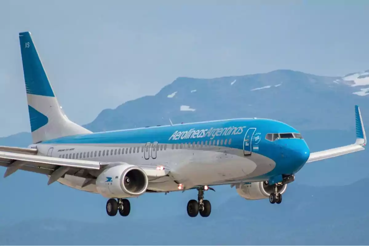 Avión de Aerolíneas Argentinas en pleno vuelo con montañas de fondo.