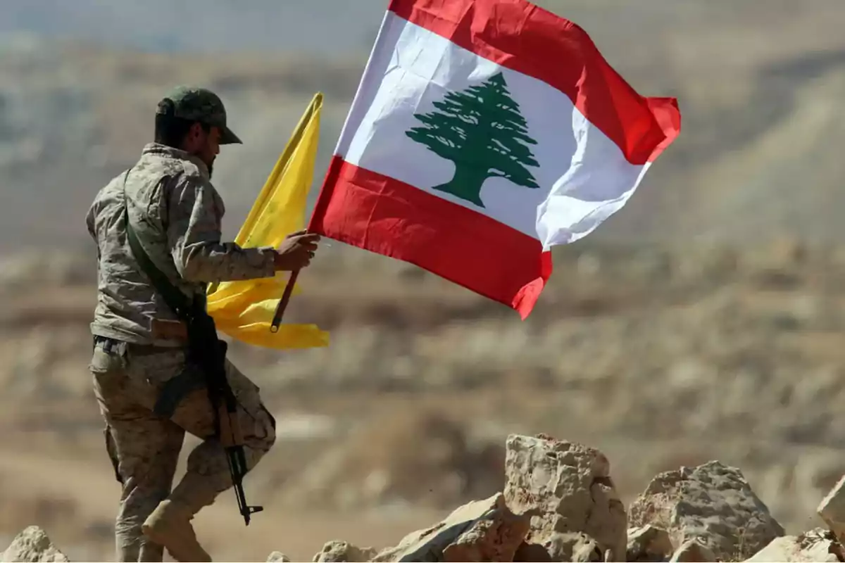 Un soldado sostiene la bandera de Líbano y otra bandera amarilla en un paisaje montañoso.