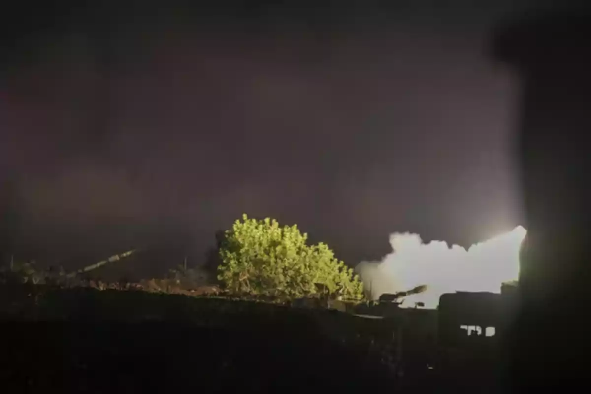 Una escena nocturna con un destello de luz y humo en un entorno oscuro con vegetación.