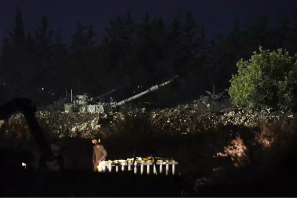 Un tanque militar estacionado en un área boscosa durante la noche con un soldado y municiones en primer plano.