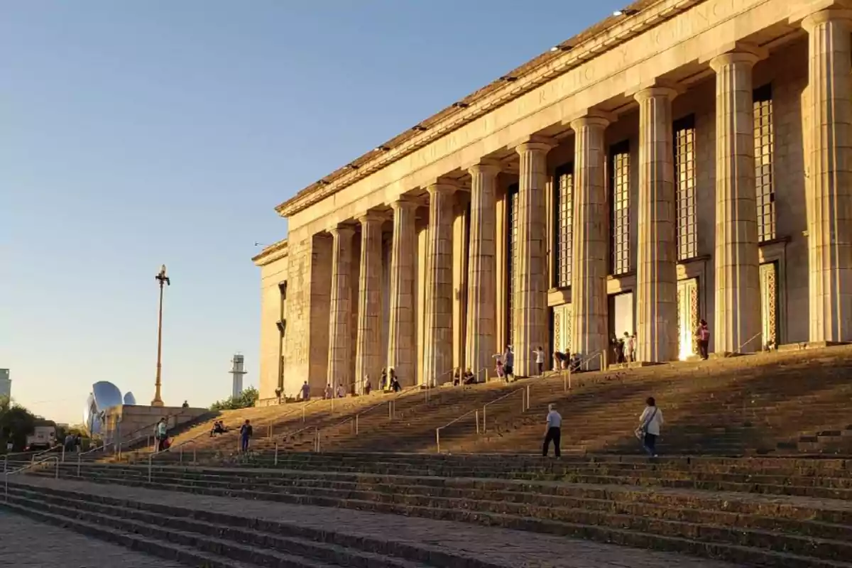 Edificio con columnas clásicas y escalinata amplia al atardecer con personas subiendo y bajando