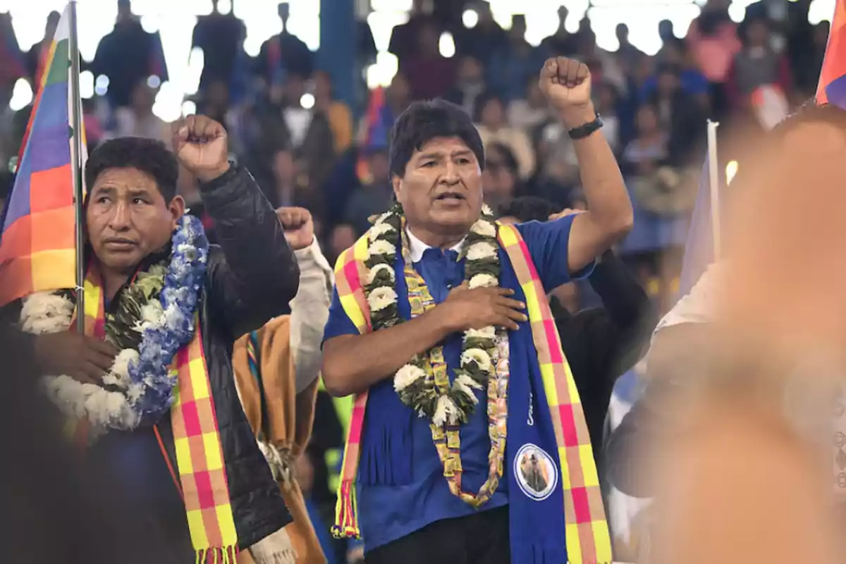 Un grupo de personas con guirnaldas y banderas coloridas levantan el puño en un evento público.