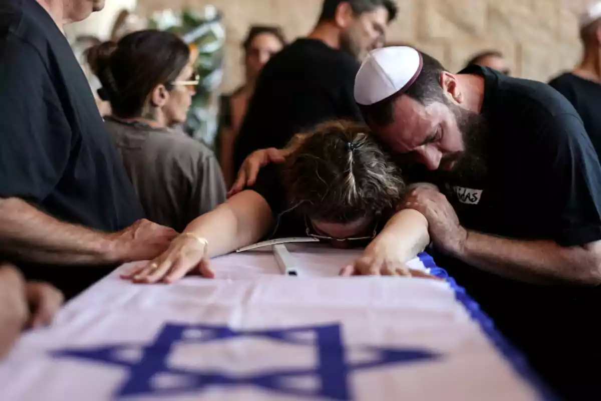 Personas en duelo se apoyan sobre un ataúd cubierto con una bandera de Israel en una ceremonia de despedida.