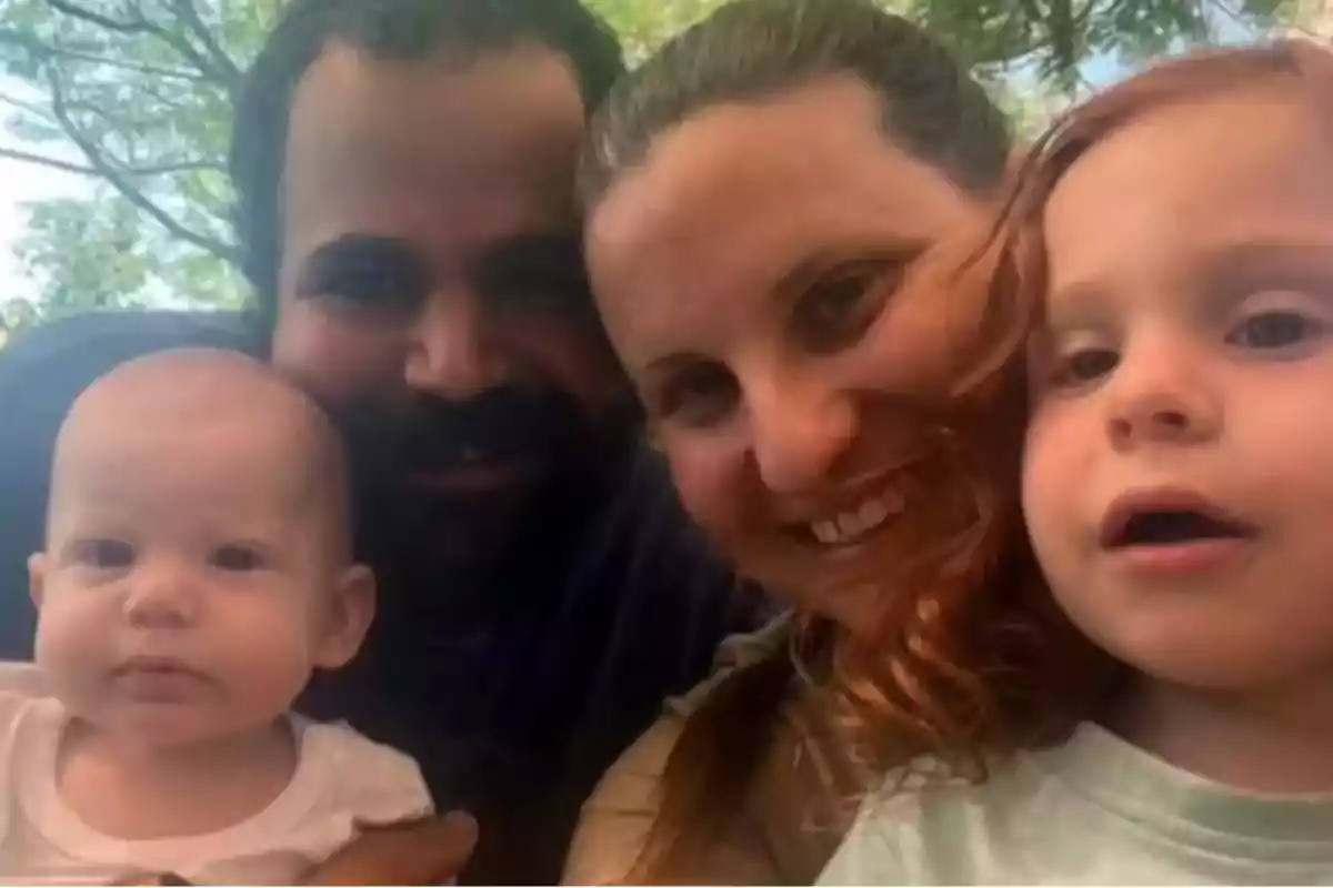 Una familia sonriente posa al aire libre con árboles de fondo.