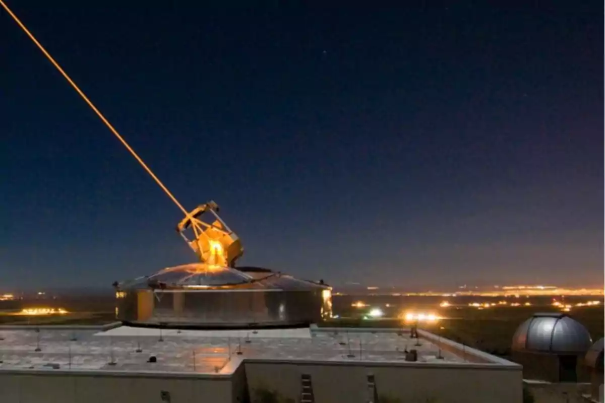 Un telescopio emite un rayo láser hacia el cielo nocturno desde un observatorio iluminado.