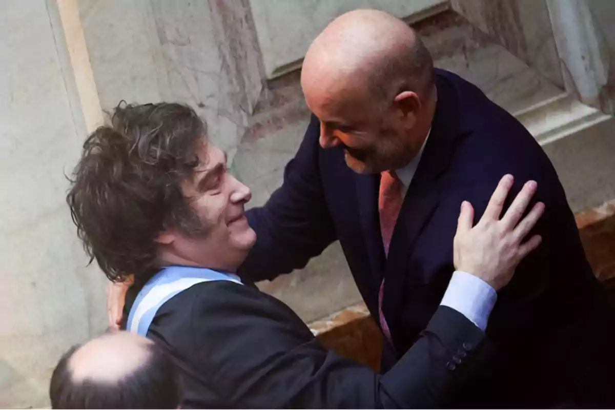 Dos hombres abrazándose y sonriendo en un entorno formal.