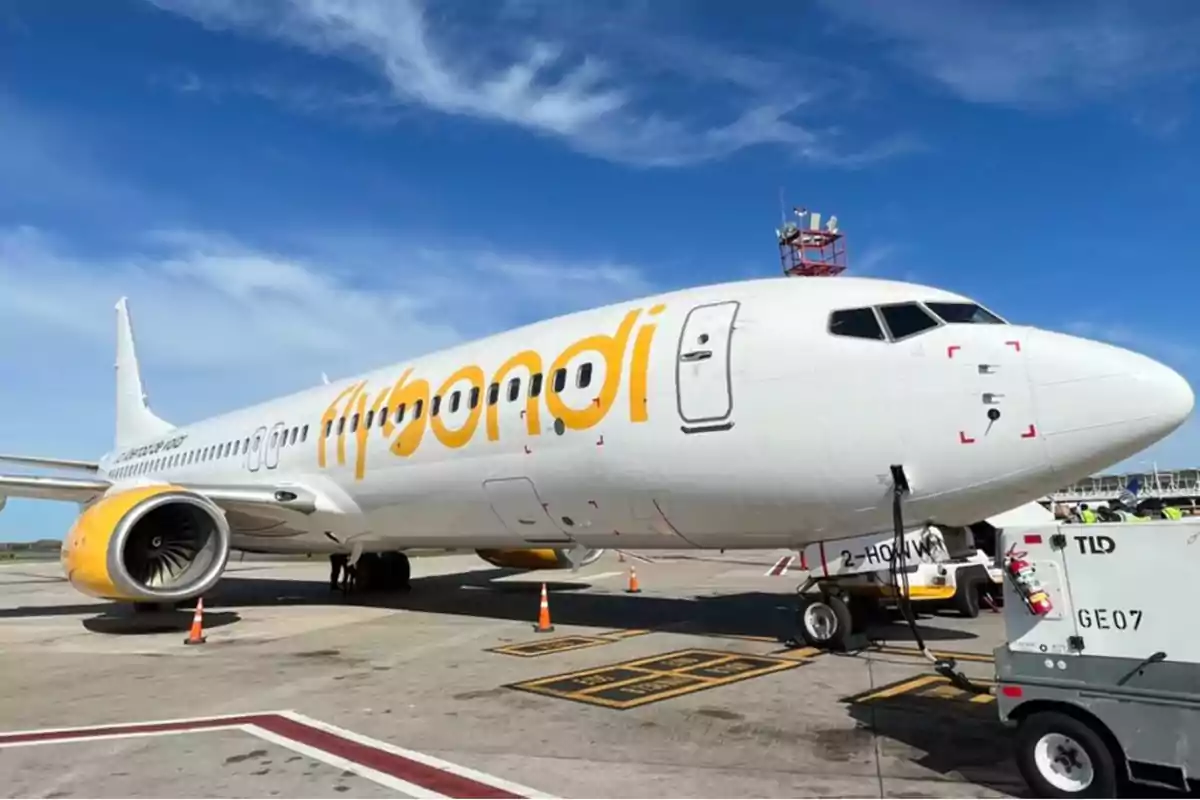 Un avión de la aerolínea Flybondi estacionado en la pista de un aeropuerto bajo un cielo azul.