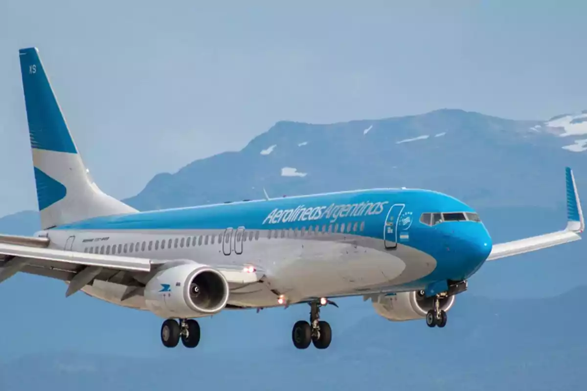 Un avión de Aerolíneas Argentinas en pleno vuelo con montañas de fondo.