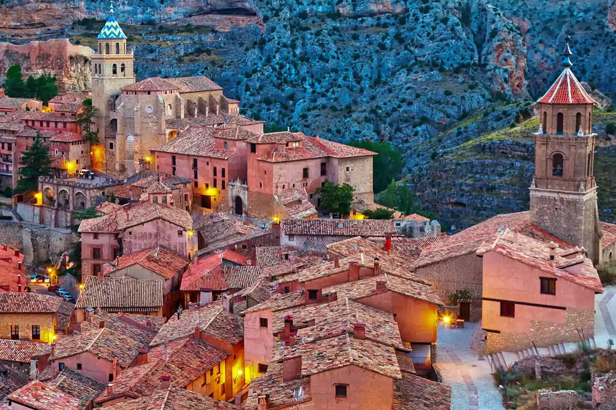 Vista panorámica de un pintoresco pueblo con casas de tejados rojos y una iglesia con torre en un entorno montañoso.