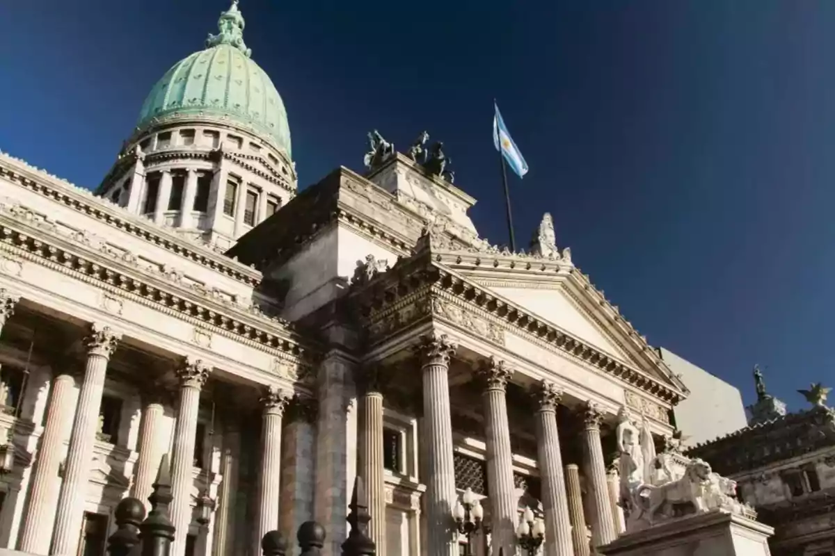 Edificio con cúpula verde y columnas clásicas bajo un cielo azul con una bandera ondeando.