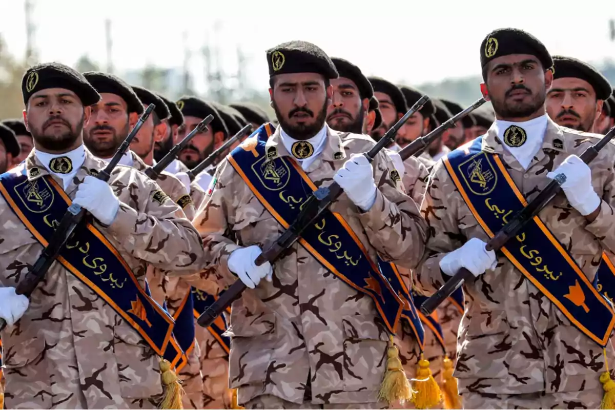 Soldados en uniforme de camuflaje marchando en formación con rifles y boinas negras.