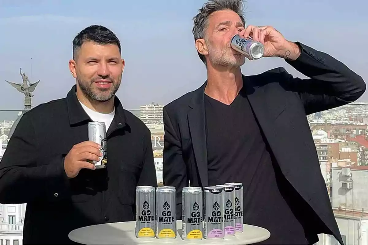 Dos personas sostienen latas de bebida Go Mate en una terraza con vista a la ciudad.