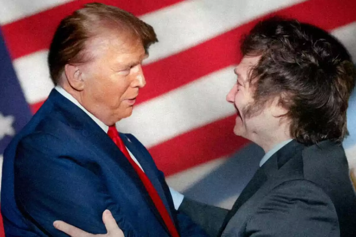 Dos personas se saludan cordialmente frente a una bandera de Estados Unidos.