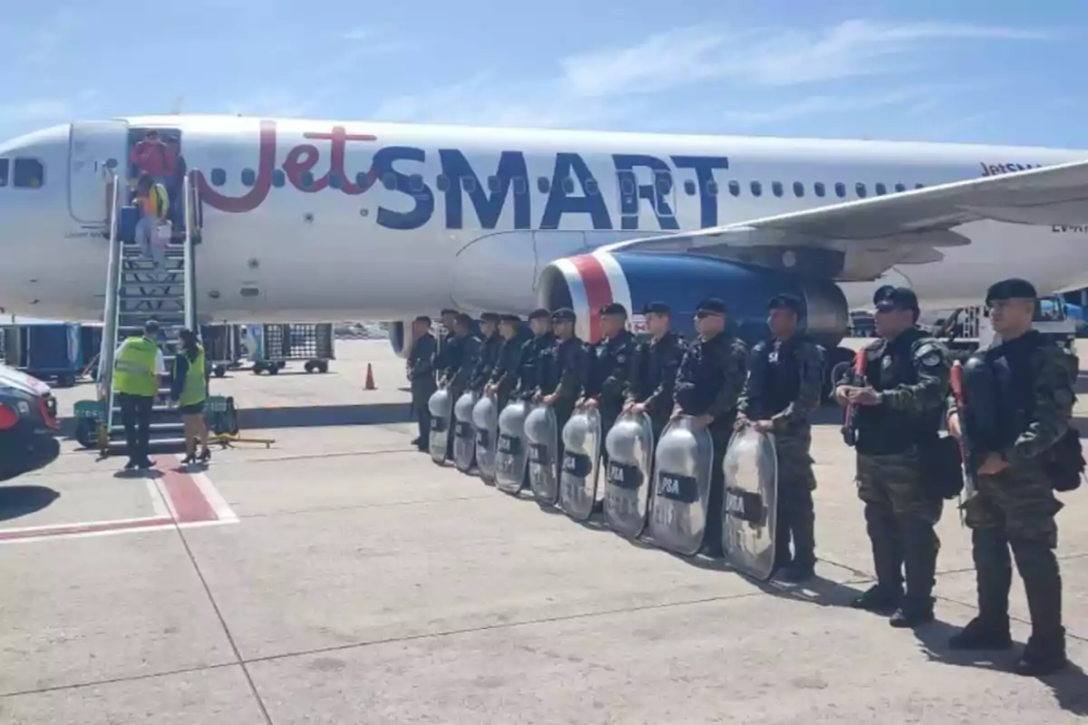 Un avión de JetSMART en el aeropuerto con personal de seguridad alineado frente a él. Un avión de JetSMART en el aeropuerto con personal de seguridad alineado frente a él.
