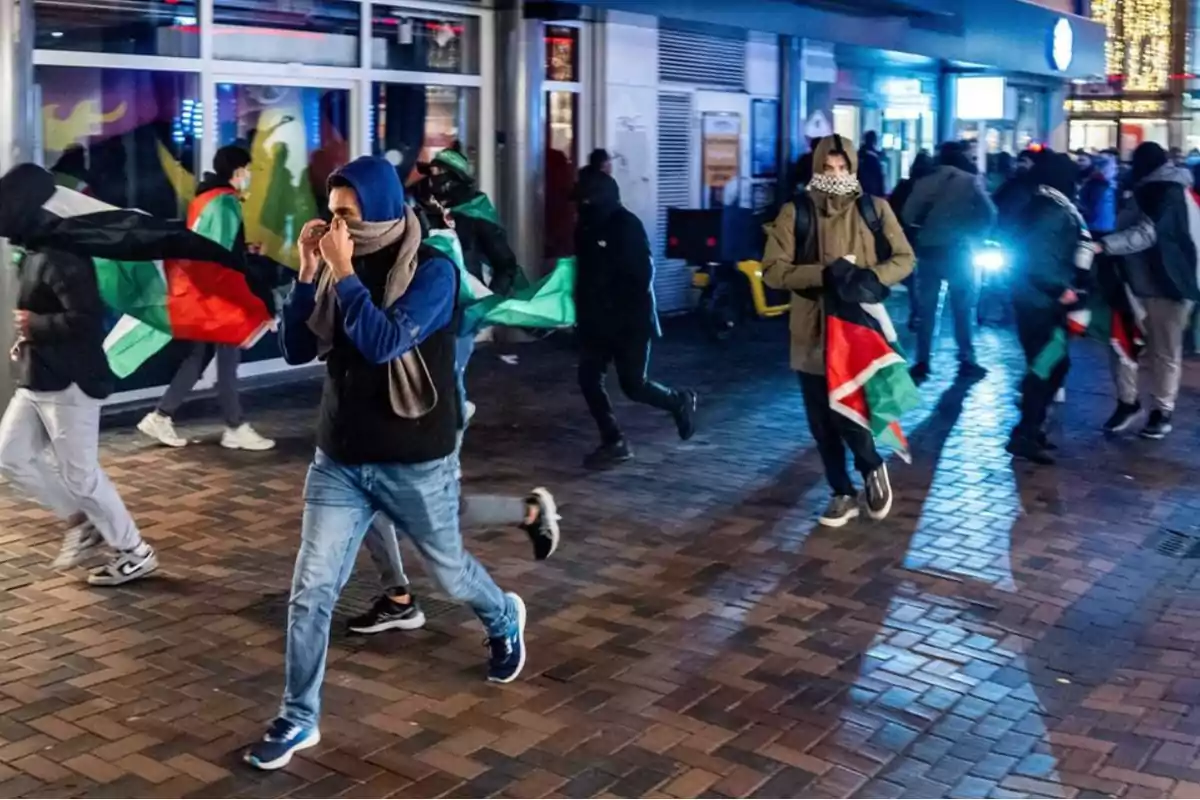 Un grupo de personas camina por una calle con banderas en la mano durante la noche.