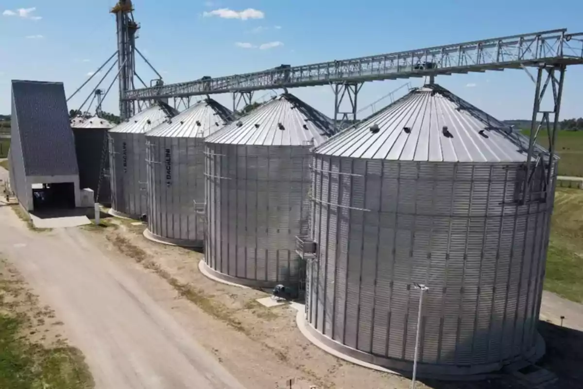 Vista aérea de varios silos metálicos en una planta de almacenamiento agrícola con un cielo despejado.