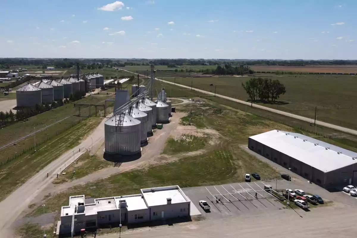 Vista aérea de una planta de almacenamiento de granos con varios silos metálicos y edificios en un entorno rural.