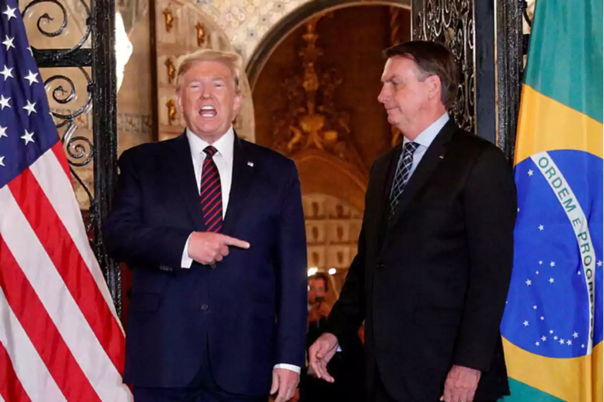 Dos hombres de traje posan junto a las banderas de Estados Unidos y Brasil en un entorno elegante.