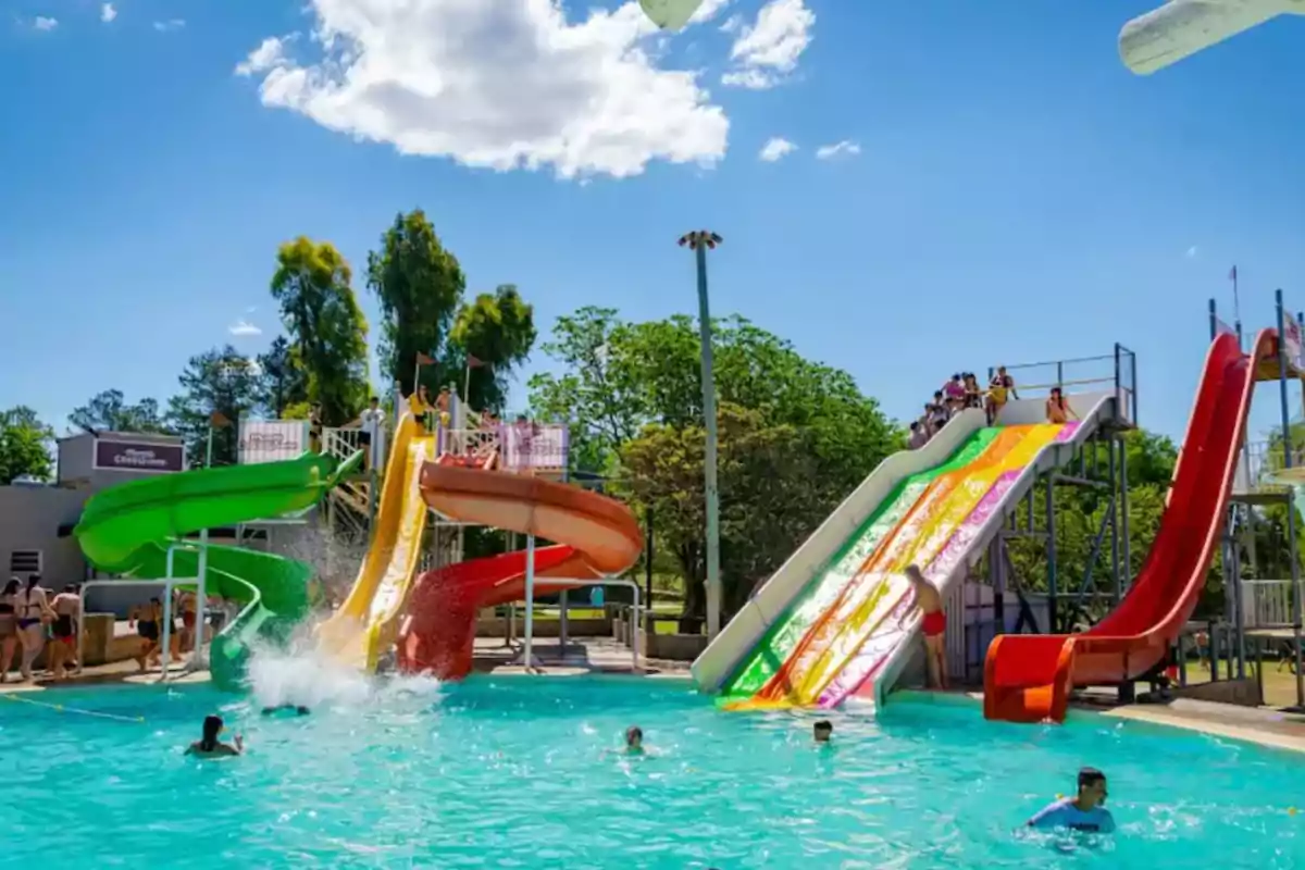 Personas disfrutando de toboganes de agua en un parque acuático bajo un cielo despejado.