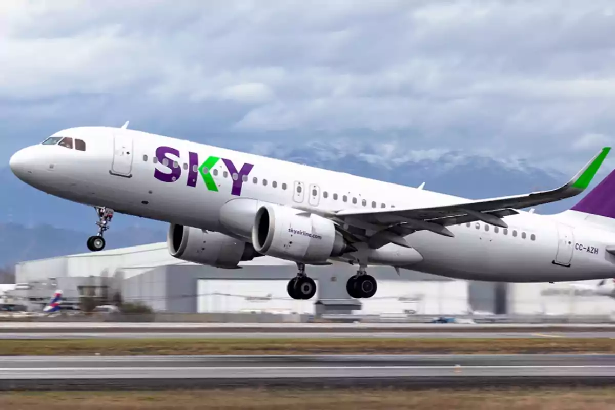 Un avión de la aerolínea SKY despegando en un aeropuerto con montañas al fondo.