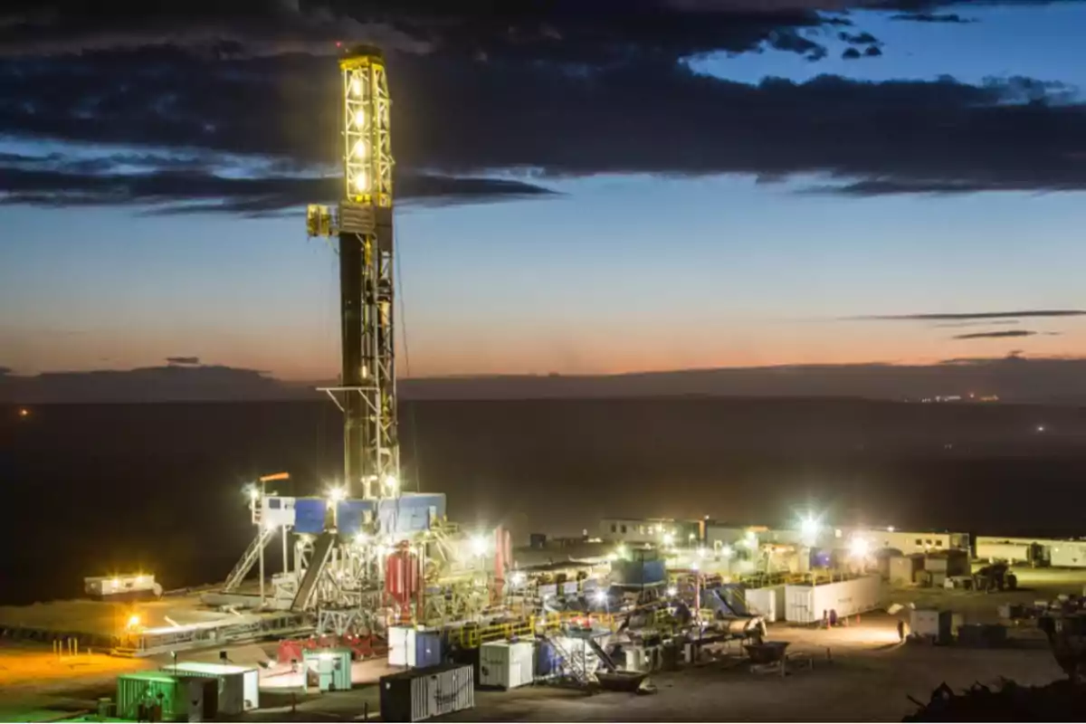 Plataforma de perforación iluminada al anochecer en un campo petrolero.