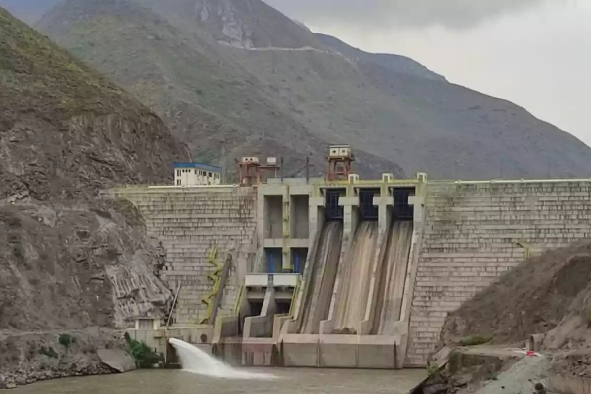 Imagen de una presa hidroeléctrica rodeada de montañas con agua fluyendo por una de las compuertas.