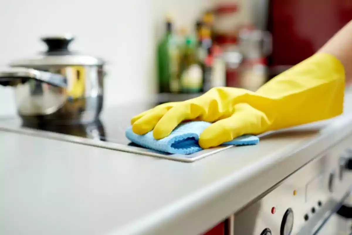 Persona limpiando una estufa con guantes amarillos y un paño azul.