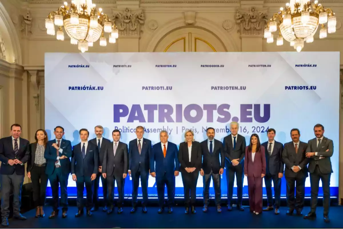 Un grupo de personas posando en un evento político con un cartel de fondo que dice 