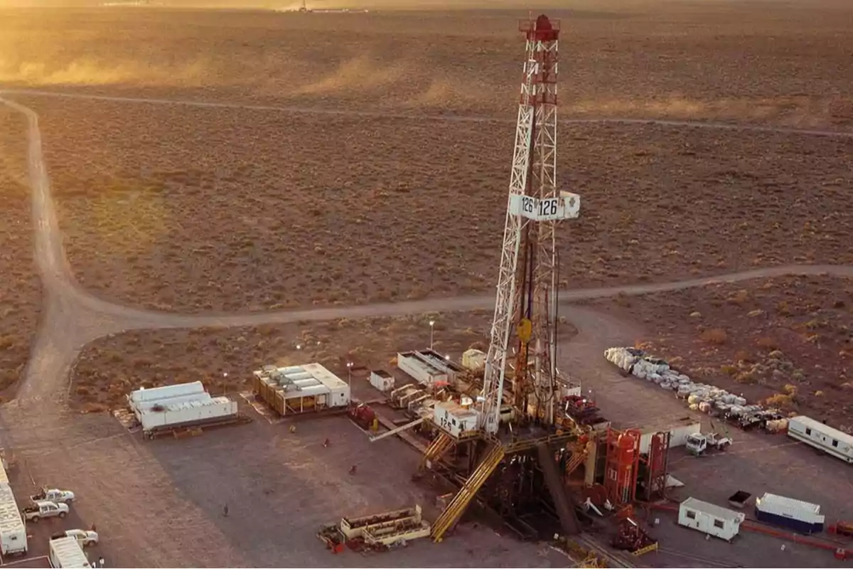 Vista aérea de una plataforma de perforación petrolera en un paisaje árido al atardecer.