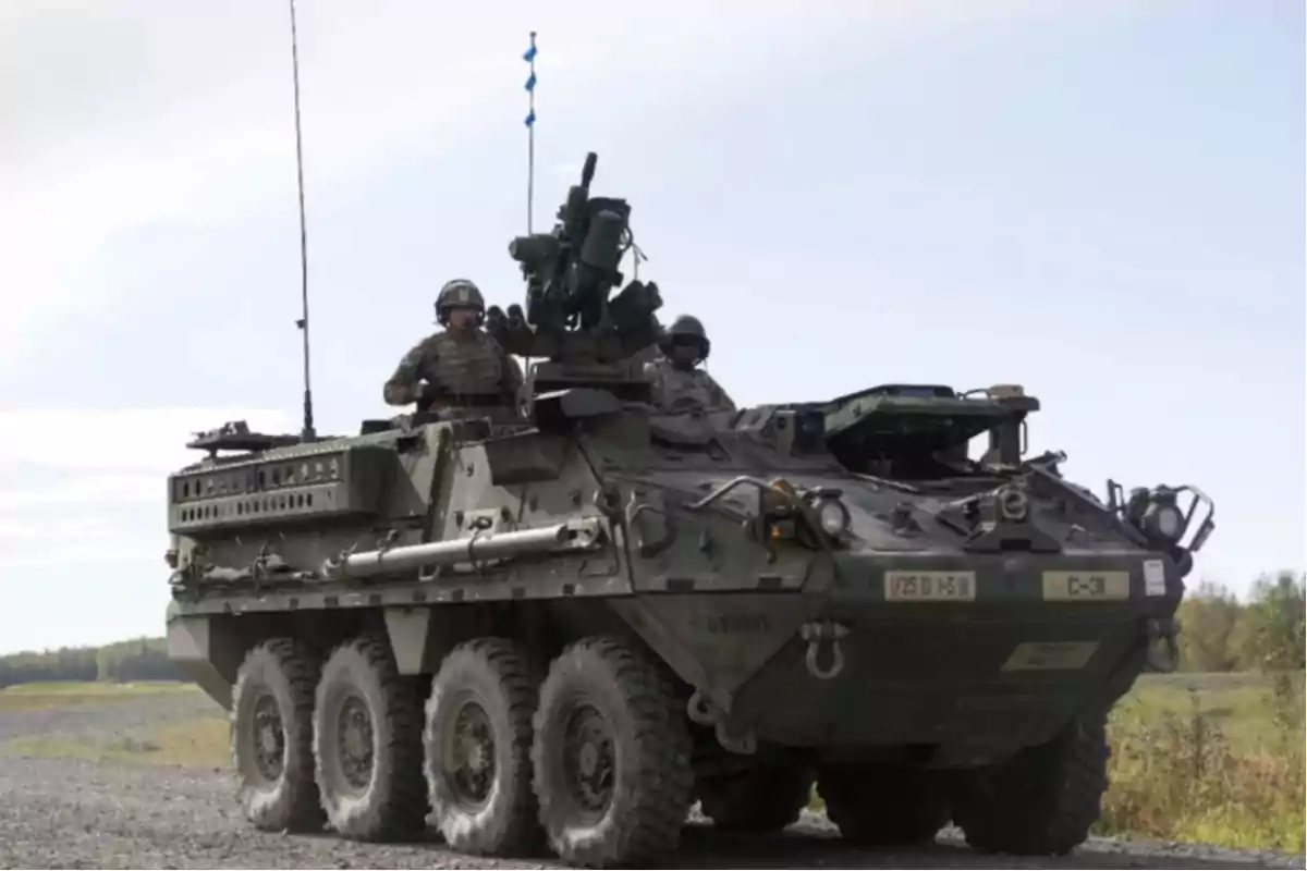 Un vehículo militar blindado con soldados a bordo circula por un camino de tierra en un entorno rural.