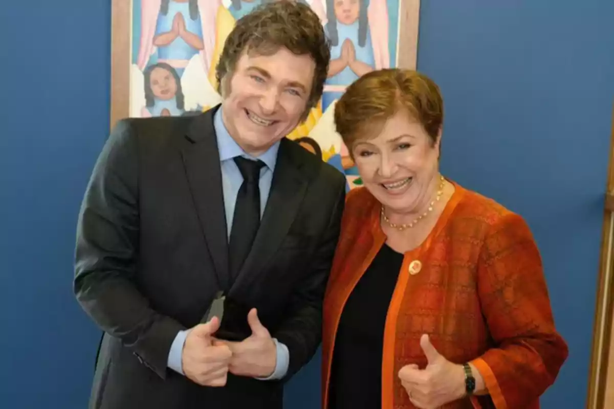 Dos personas sonriendo y levantando el pulgar, con un cuadro colorido de fondo.