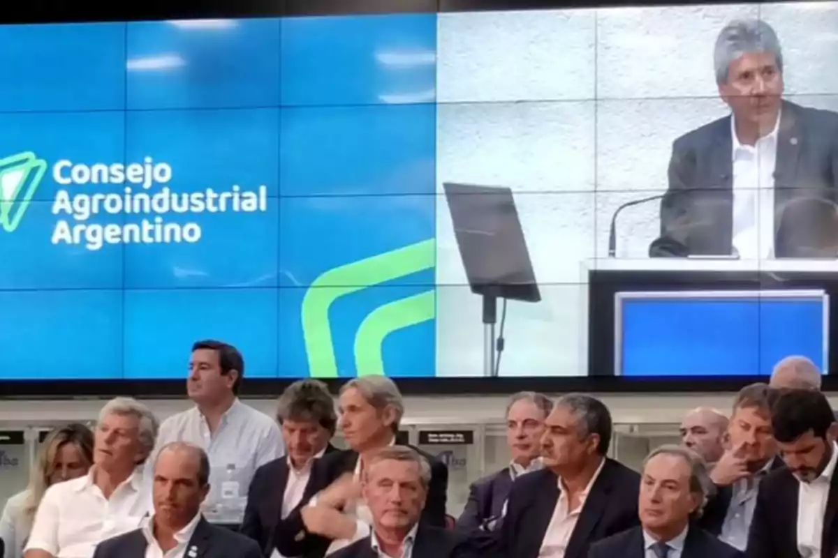 Un grupo de personas asiste a un evento del Consejo Agroindustrial Argentino, con un orador en un podio y una pantalla de fondo que muestra el logotipo de la organización.