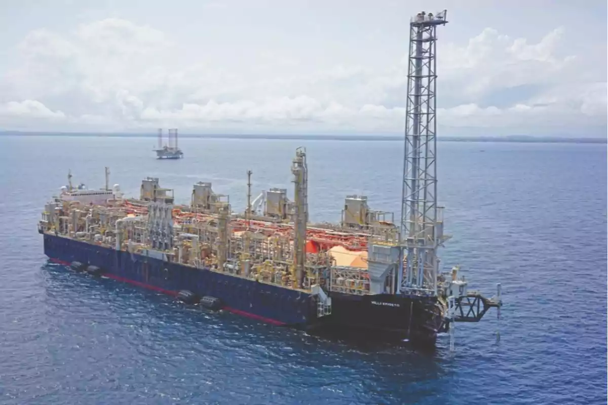 Plataforma flotante de producción de gas natural en el océano con una estructura de perforación visible y otra plataforma en el horizonte.